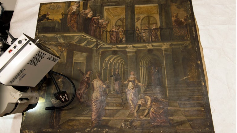 A large painting, by Tintoretto shows a group of women inside a classical building, some are looking over a balcony. A microscope is positioned over part of the painting.